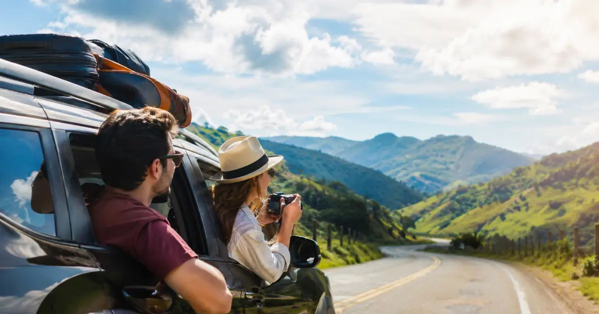 Pareja asomada por la ventana de un auto mirando una carretera de montaña en un viaje de puente